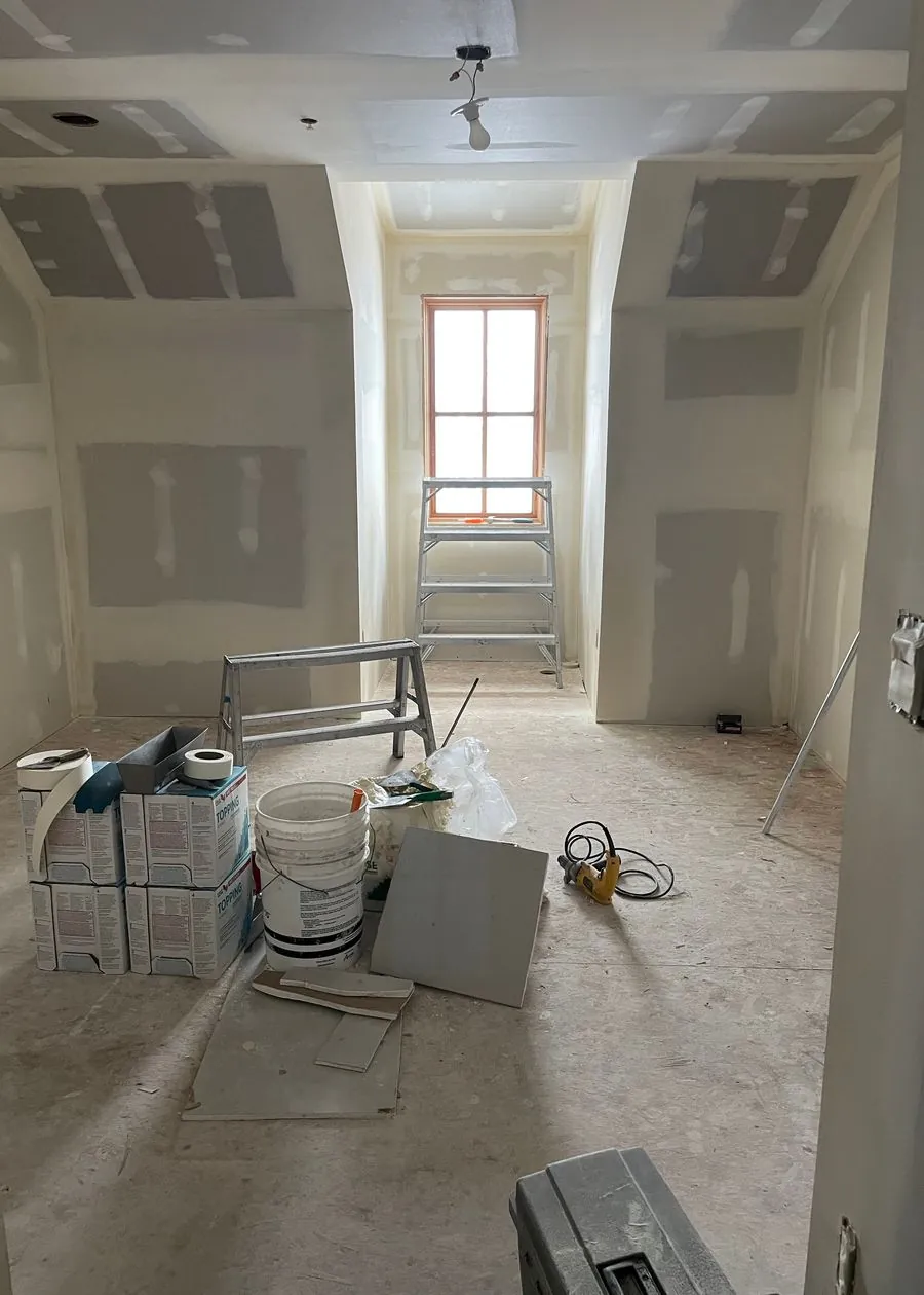 A room mid-build after drywall, with a ladder and finishing supplies